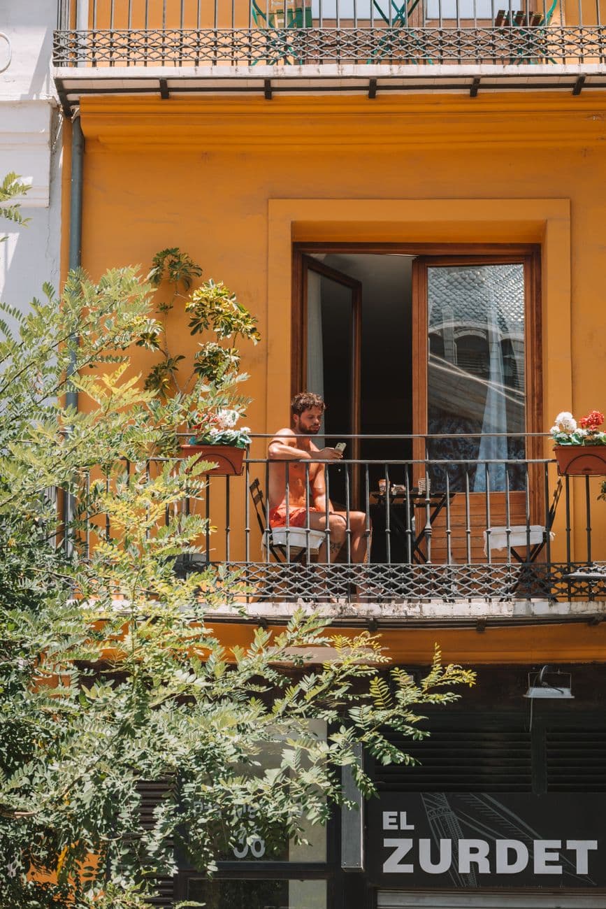 Summer scene of a man sitting on a balcony in Valencia, Spain, enjoying a sunny day.