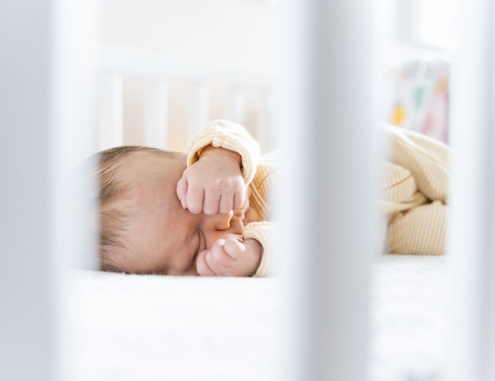 A serene sleeping baby rests peacefully in a bright and cozy crib, framed by white bars.