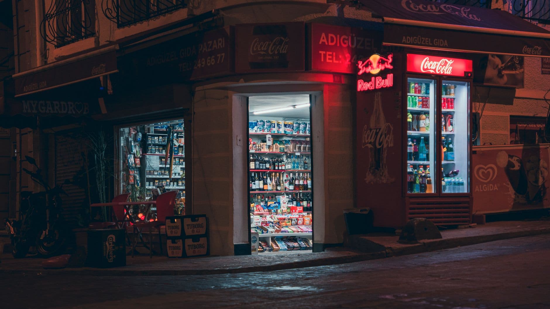A cozy corner store at night, illuminated by vibrant neon signage and streetlights.