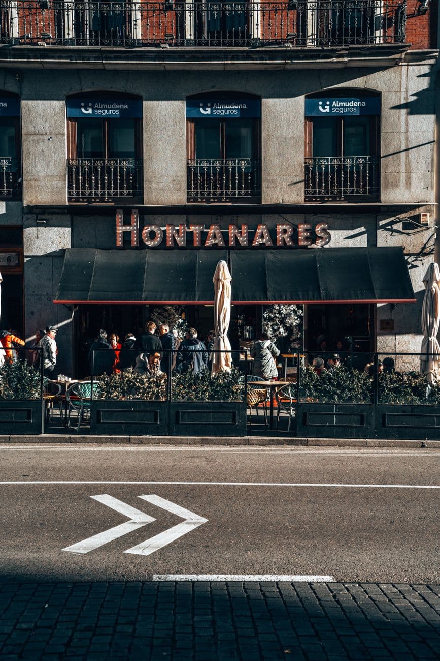 Quaint terrace cafe with patrons enjoying a sunny afternoon in a historic city street.