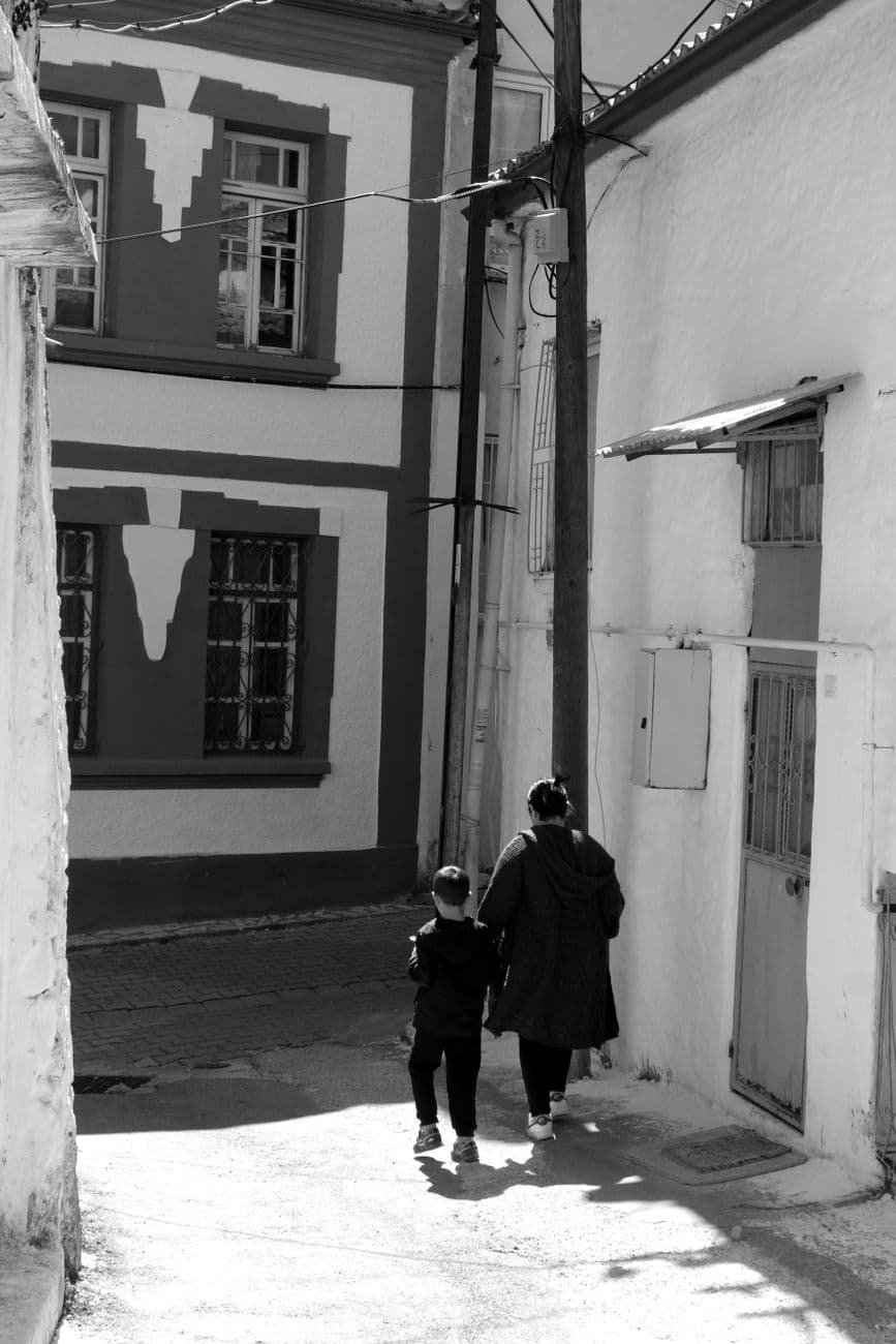 Black and white scene of a mother and child walking in a traditional street in Muğla, Türkiye.
