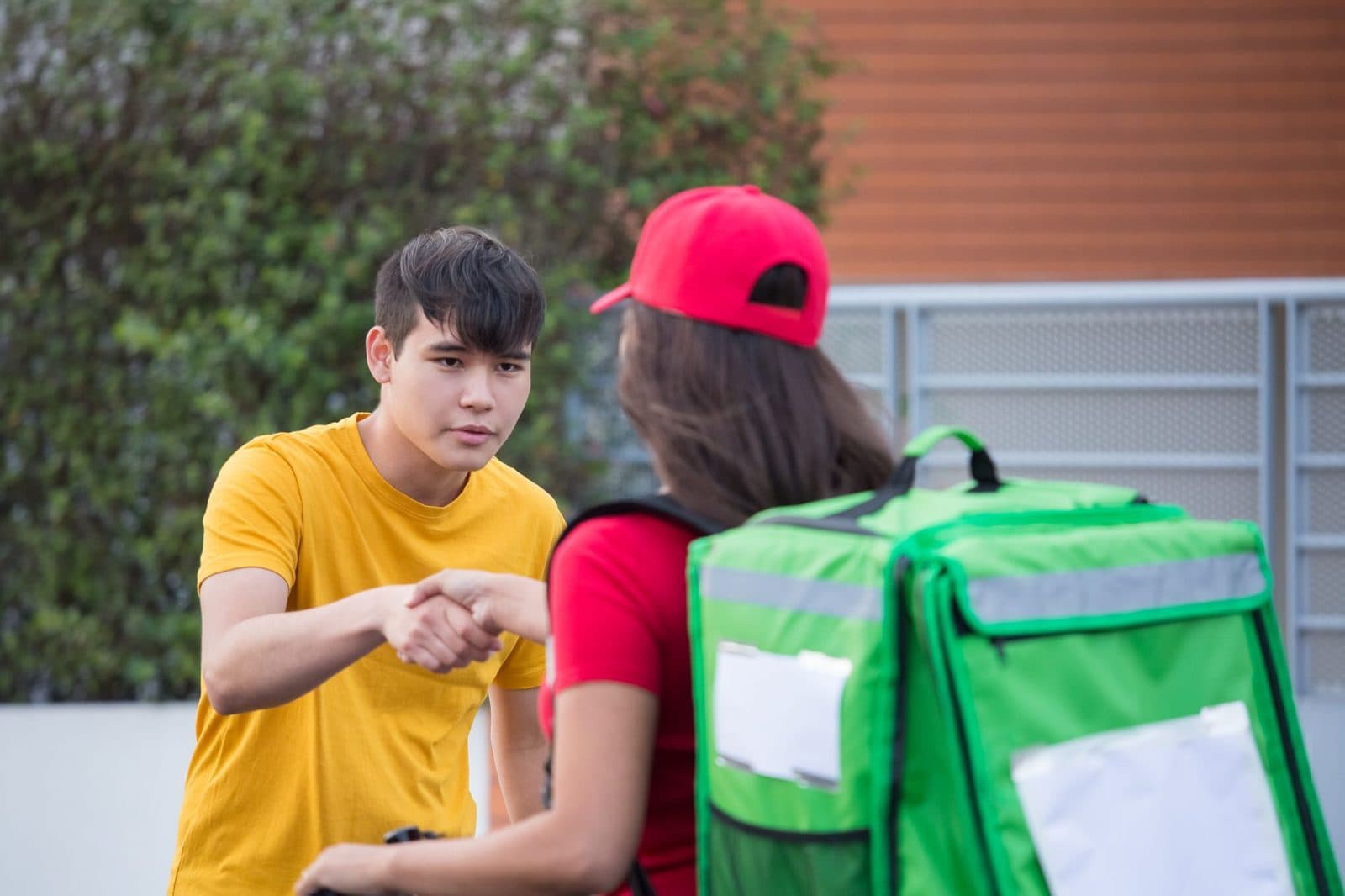 A delivery person in uniform shaking hands with a customer outdoors, representing delivery service.