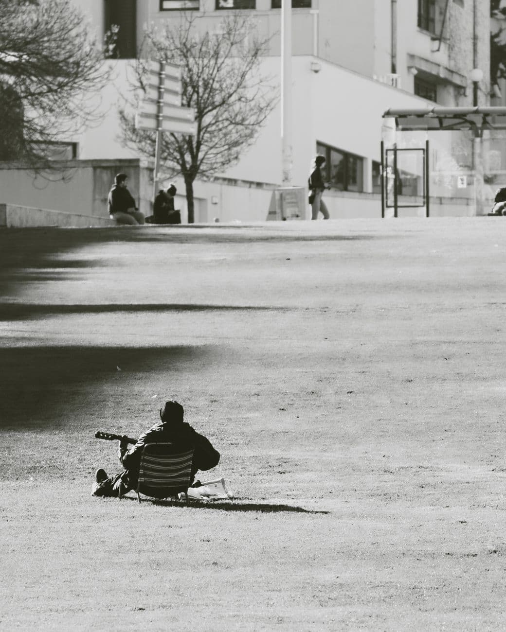 A person playing guitar in a peaceful city park, captured in black and white.