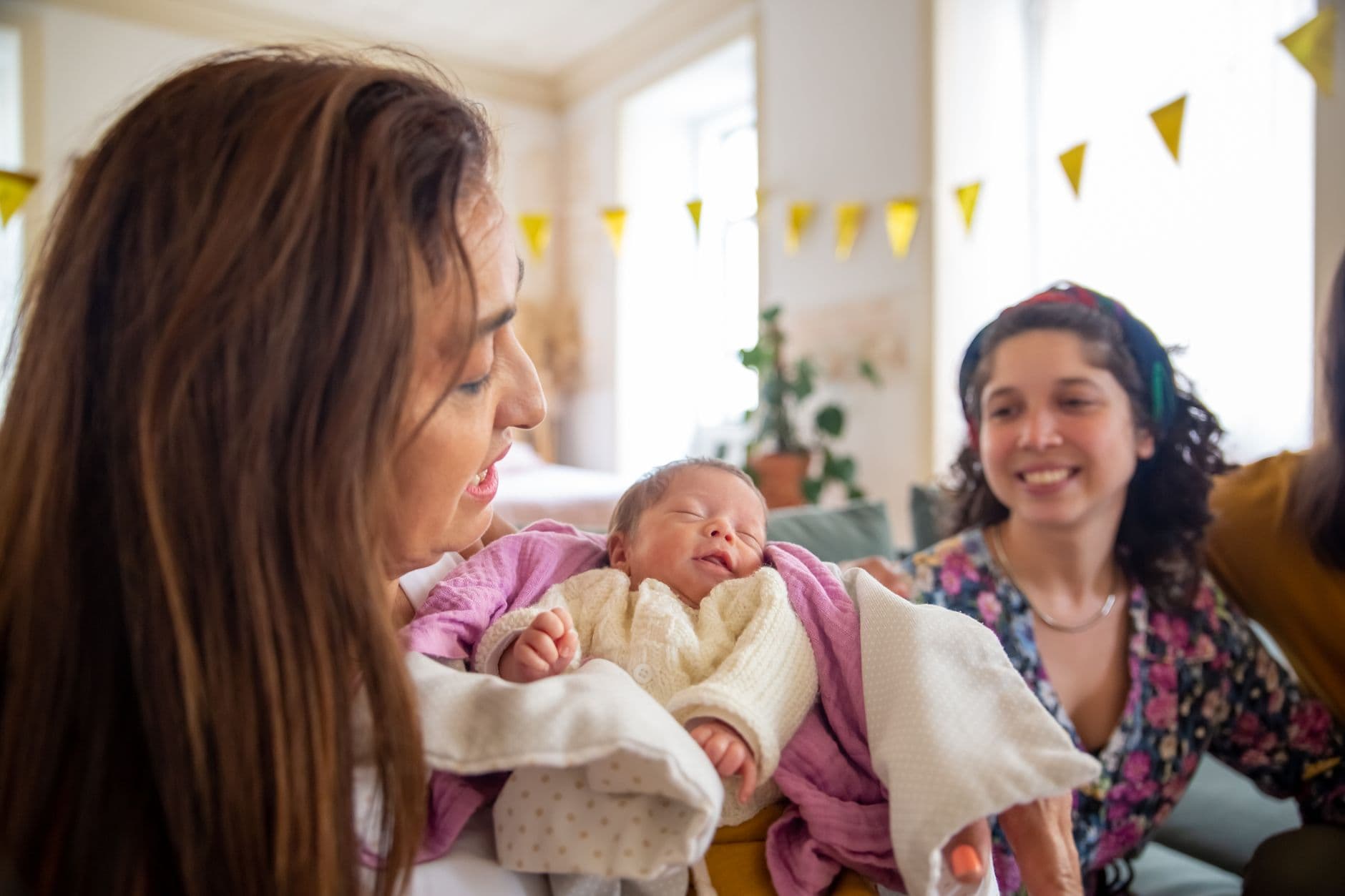 Mother lovingly cradles her newborn baby, celebrating with family indoors.