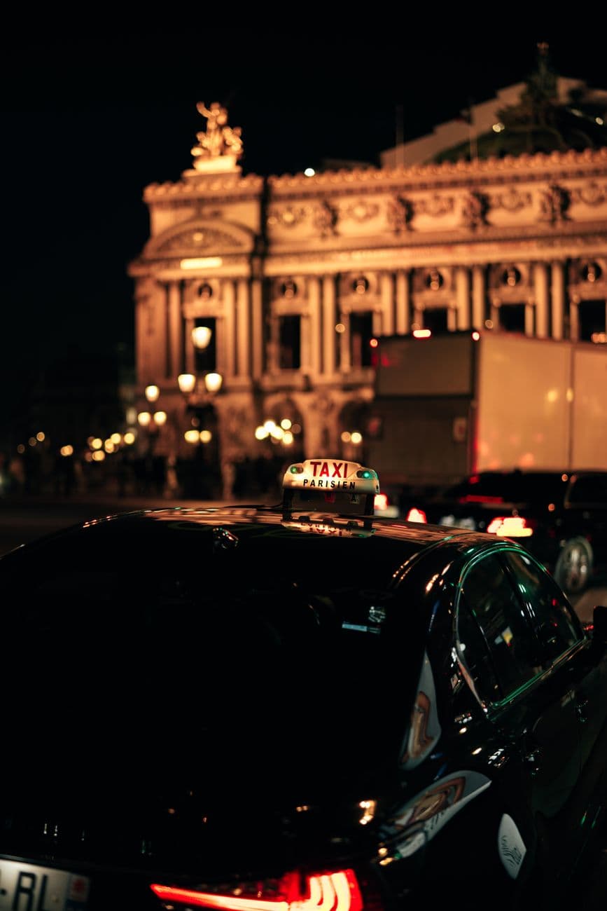 Illuminated Opera Garnier at night with a taxi in the bustling streets of Paris.