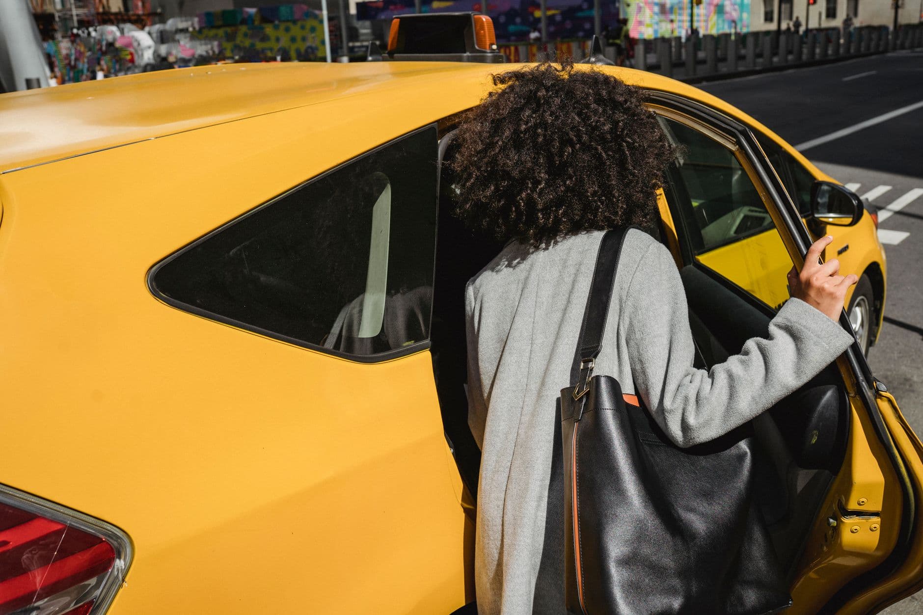 Back view of faceless ethnic female in casual clothes opening door and getting in cab in modern city