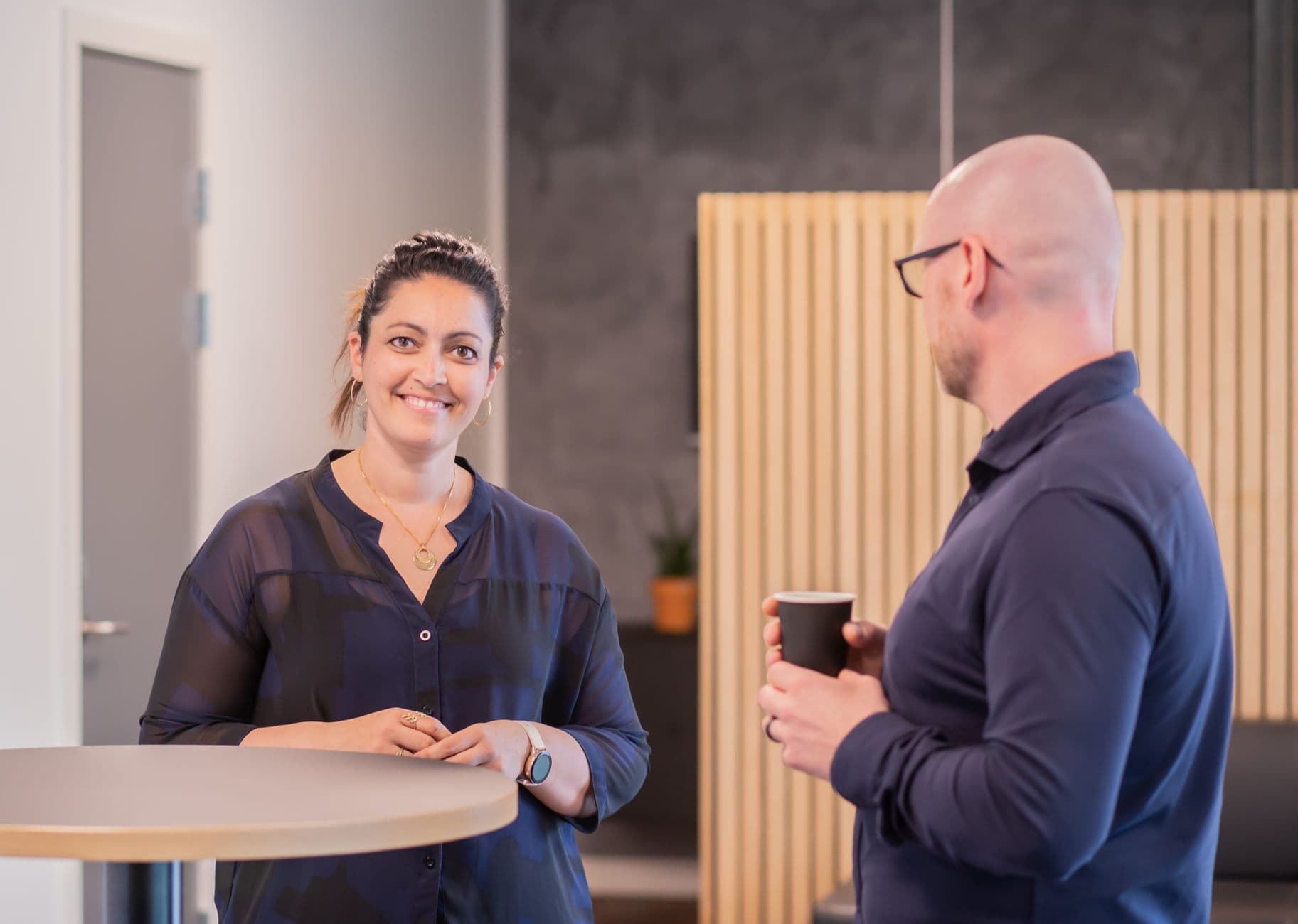Two colleagues enjoying a casual conversation during a coffee break in a modern office setting.