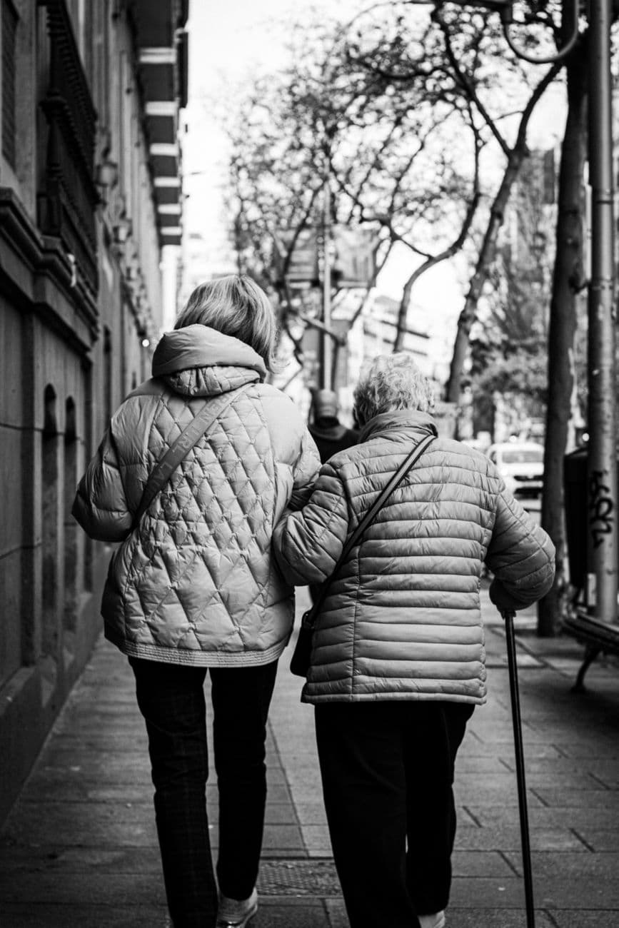 Two women, one elderly and one middle-aged, walking together on a Madrid street, highlighting companionship.
