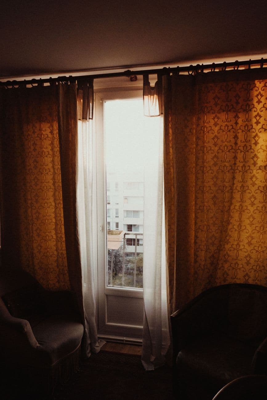 Sunlight illuminates a Parisian room with elegant curtains and armchairs.