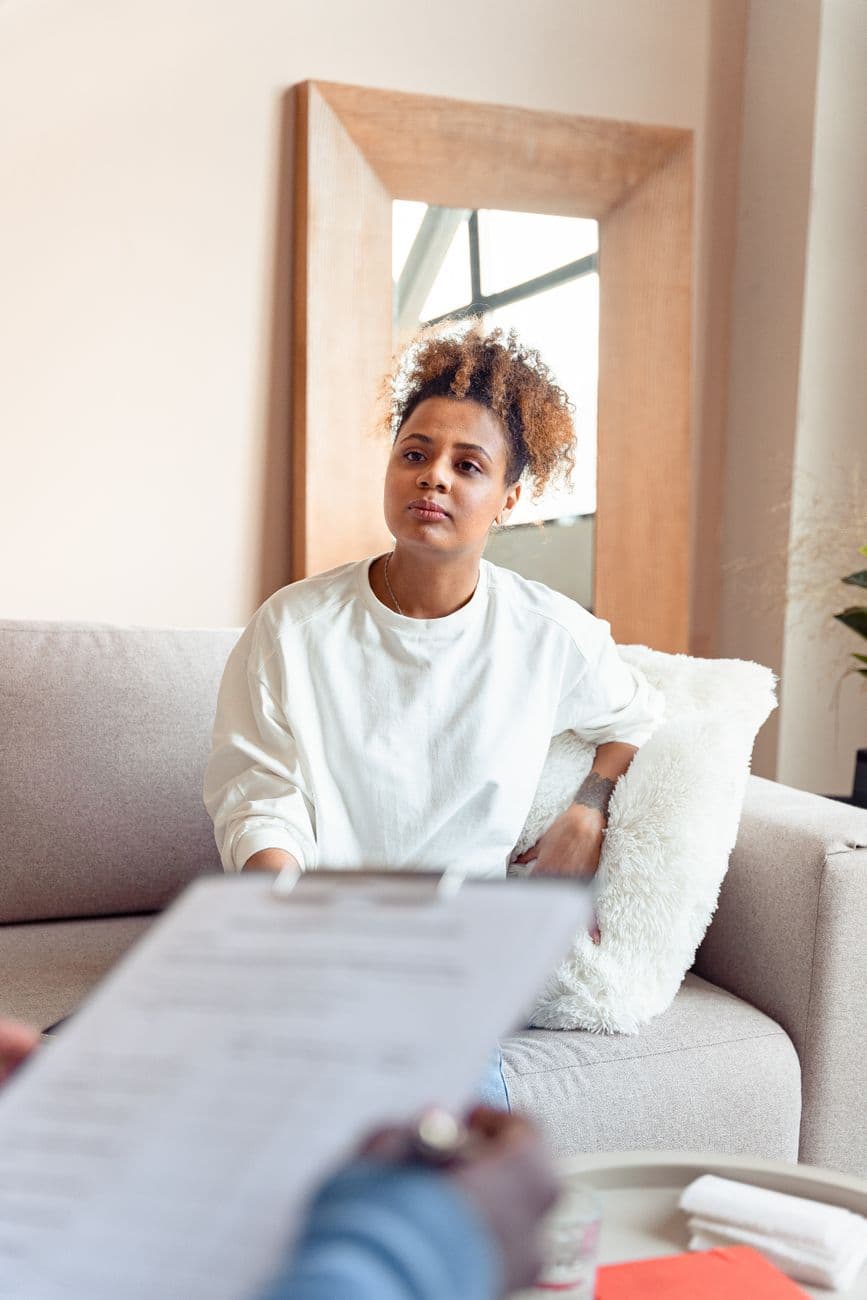 A woman engages in a thoughtful discussion during a therapy session, seated on a couch.