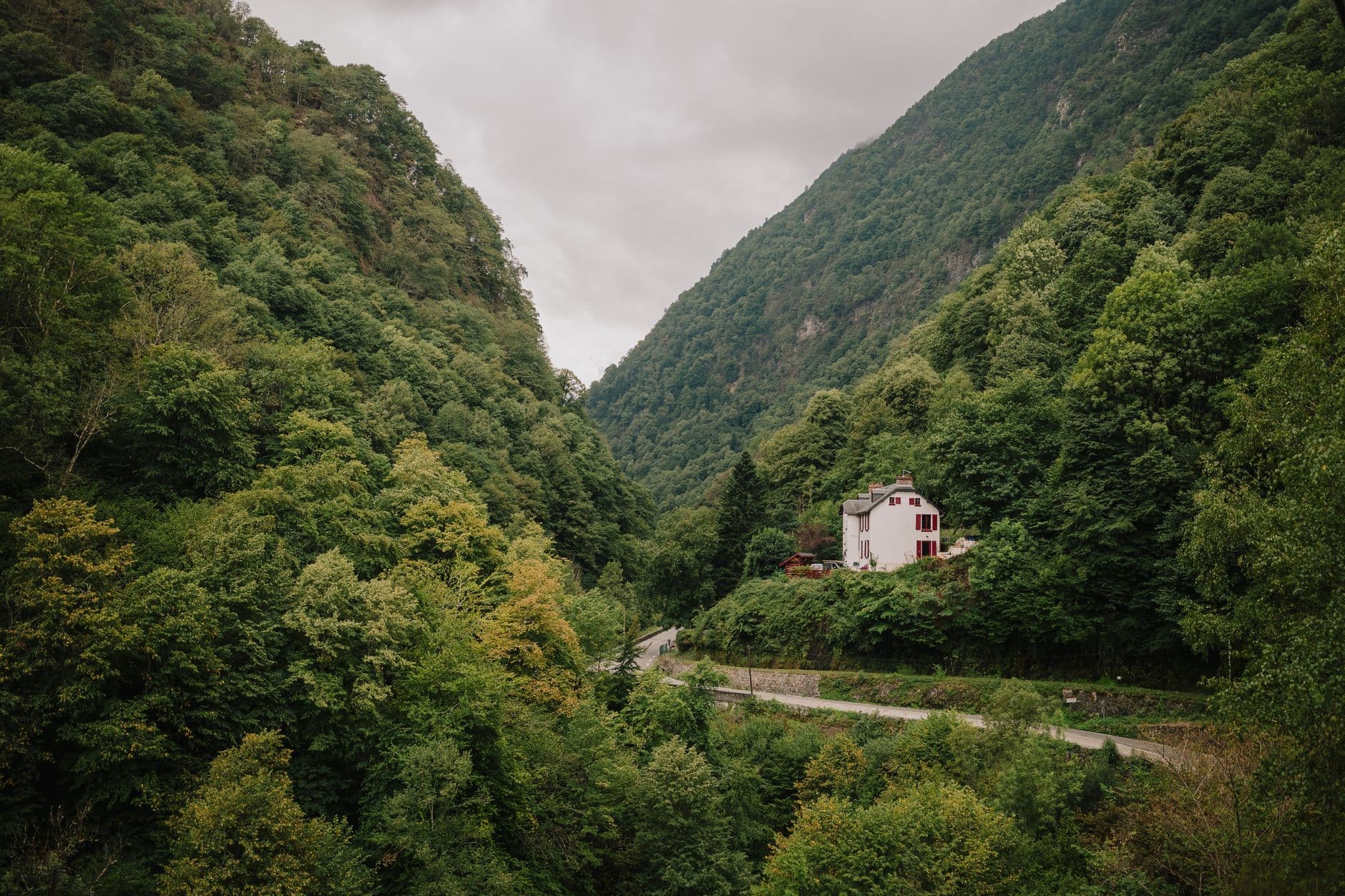 A picturesque house nestled between verdant hills in Cauterets, France, under a cloudy sky.