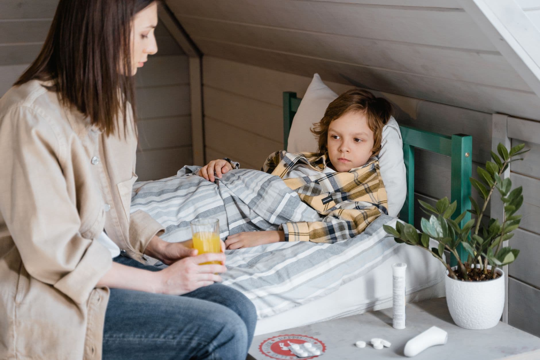 A caring mother gives orange juice to her child resting in bed, providing comfort and care.
