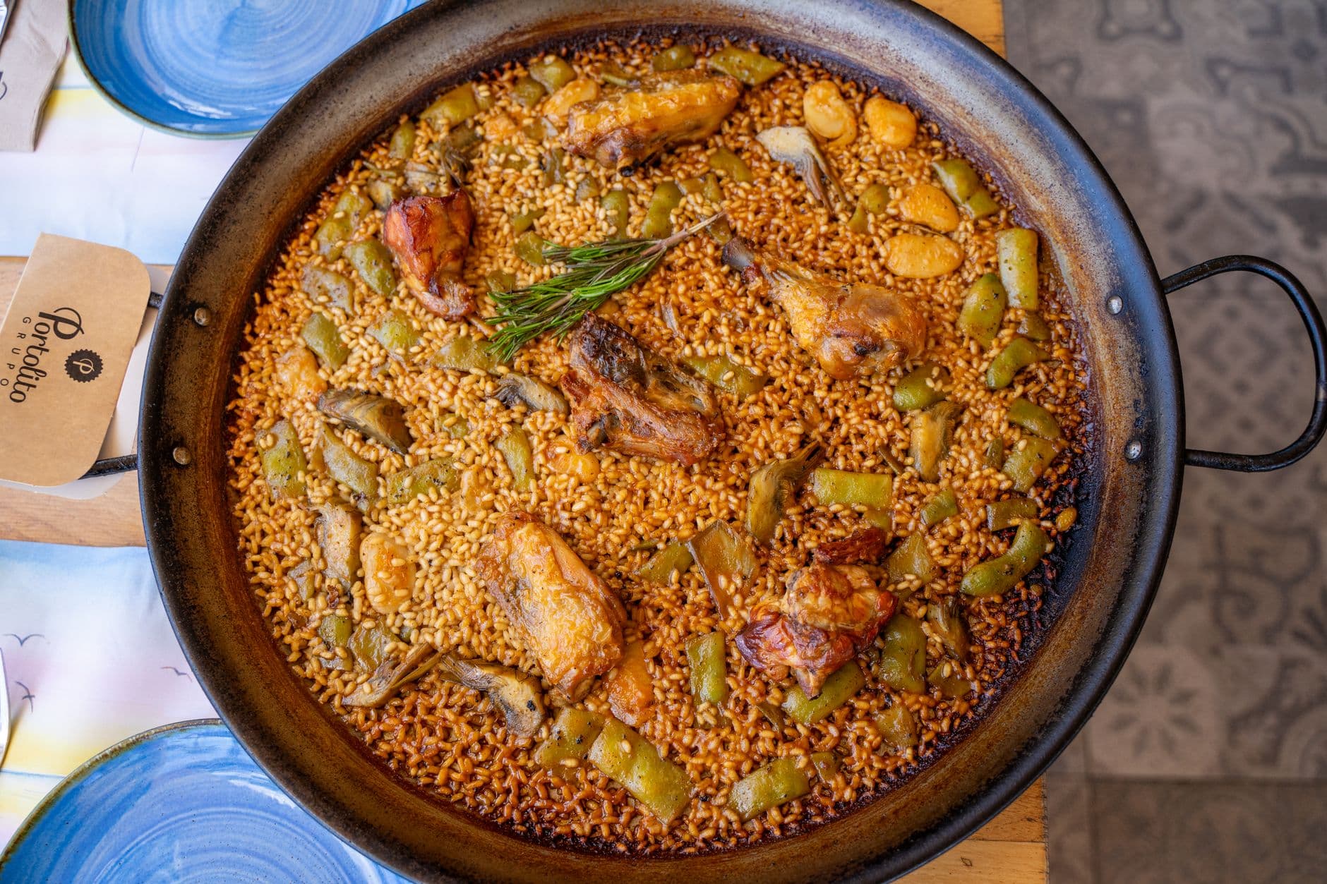 Authentic Valencia paella in a pan with chicken, vegetables, and rosemary. Top view.