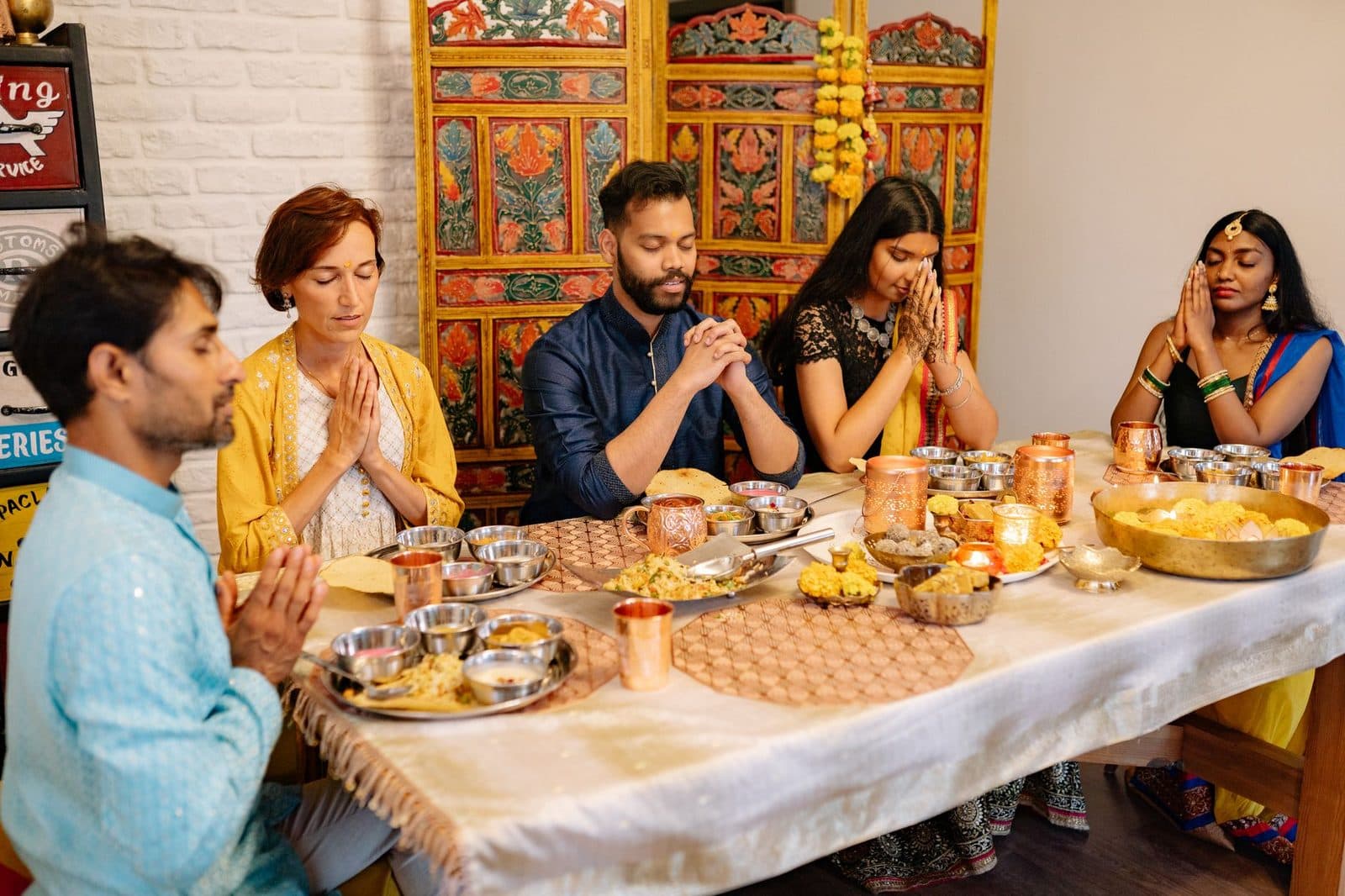 A family around a dinner table praying together during Diwali celebration, indoors.