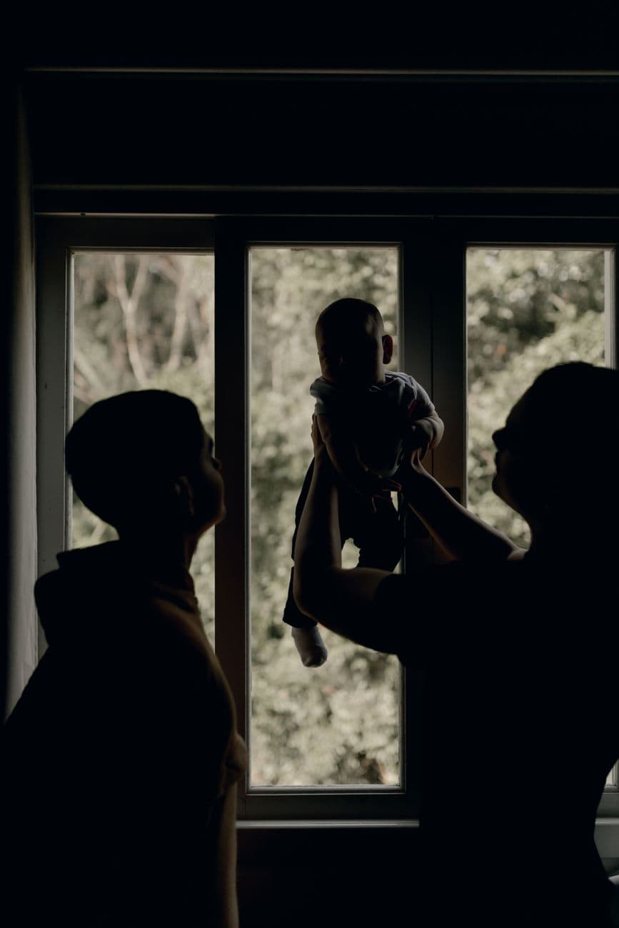 Silhouette of family embracing a baby in front of a window during daytime.