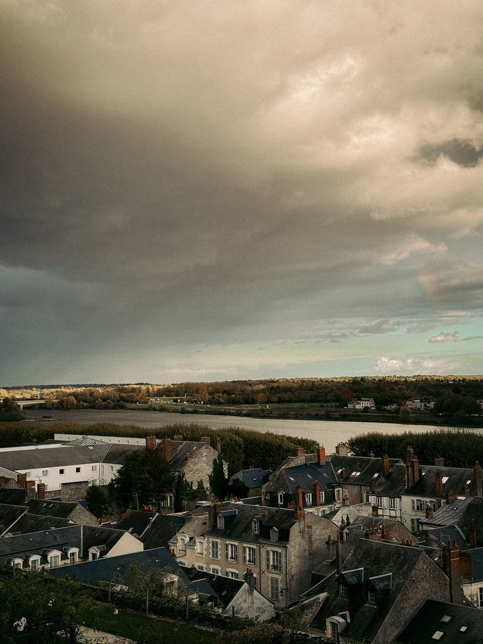 A captivating view of a French town with dramatic clouds overhead, showcasing intricate rooftops and a serene landscape.