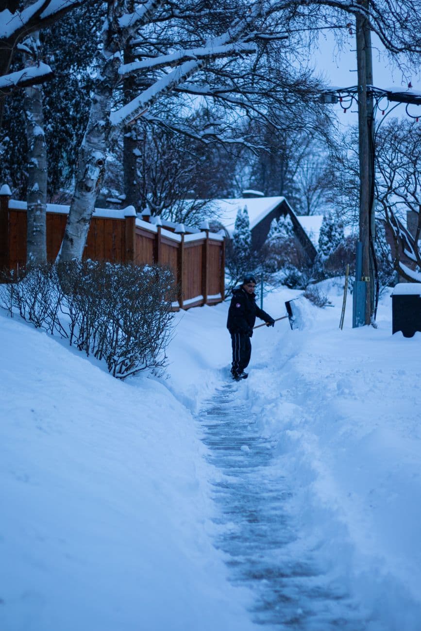 Person shoveling snow on a residential sidewalk during a winter morning in Toronto, Canada.