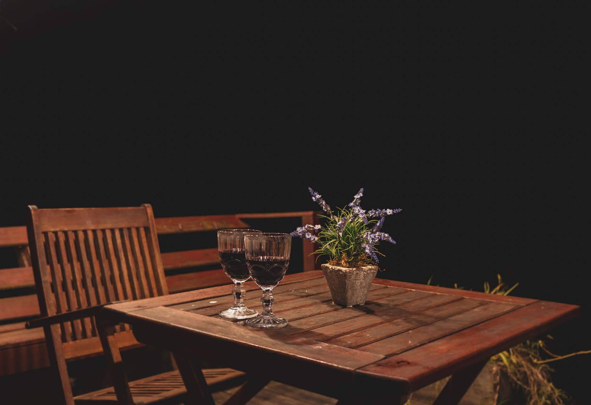 Cozy wooden table at night with two wine glasses and a lavender plant.