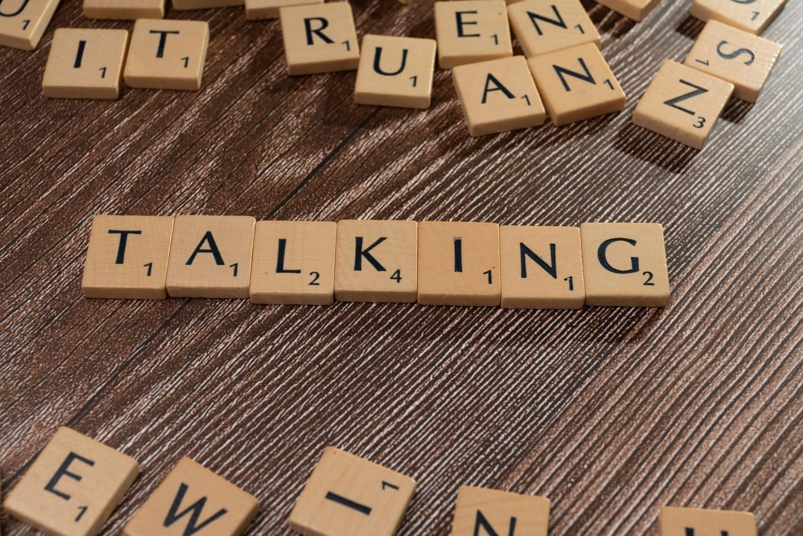 Scrabble tiles spelling 'Talking' on wooden surface, symbolizing communication.