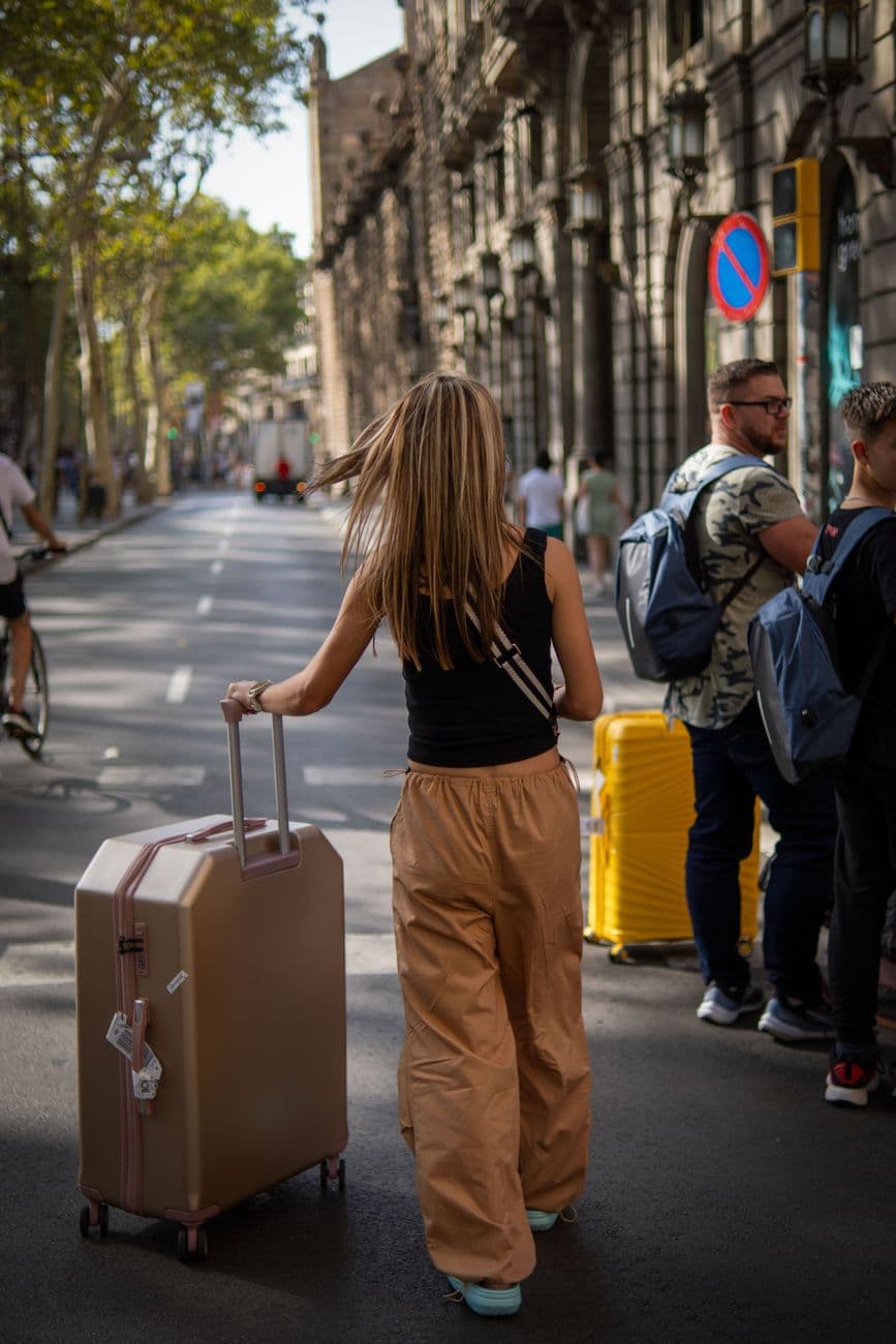 Travelers with luggage walking on a sunny city street in summer.