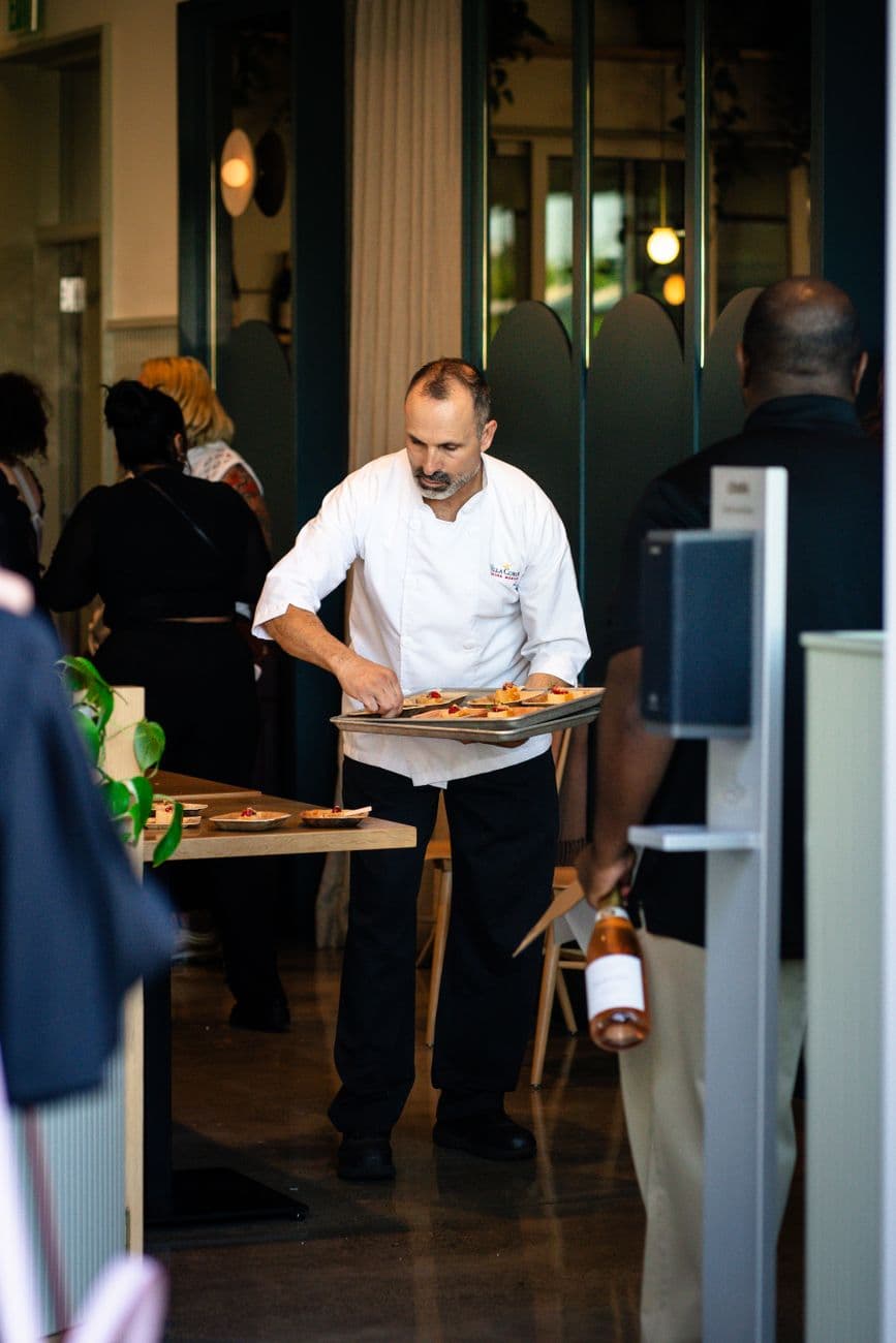 Chef presenting dishes to customers in a lively restaurant setting, showcasing hospitality.