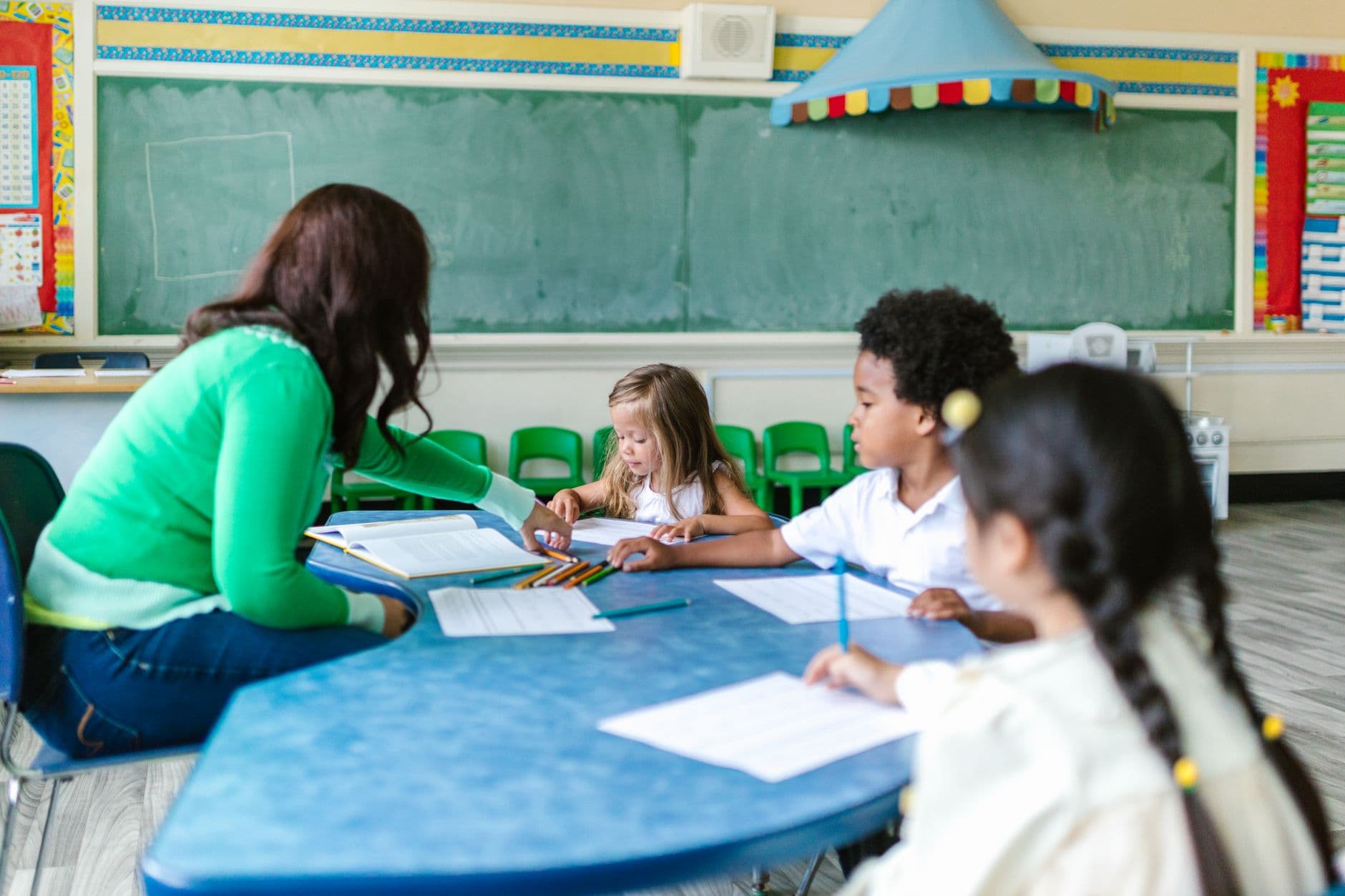 Preschool children engaged in learning with a teacher in a classroom setting.