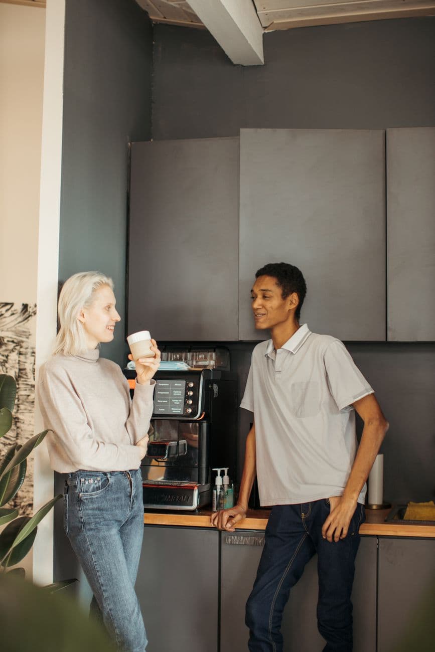 Two colleagues conversing over coffee in a creative office space. Relaxed atmosphere indoors.