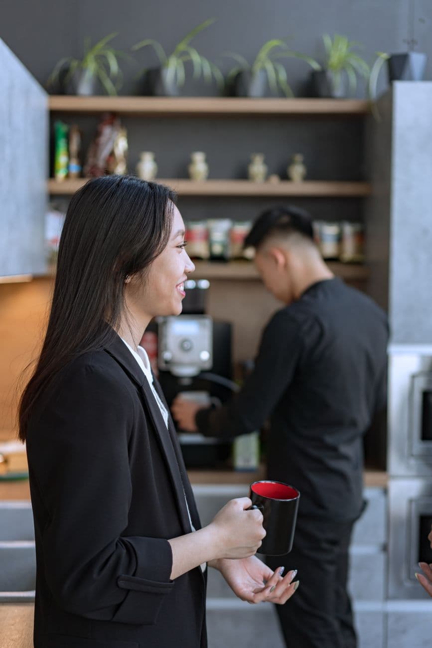 Two colleagues enjoying a coffee break in an office kitchen setting, sharing smiles and conversation.